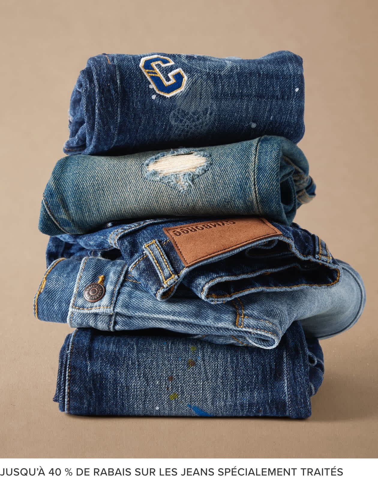 Une pile de divers vêtements en denim, notamment des jeans, des vestes et une serviette, sur un fond beige.