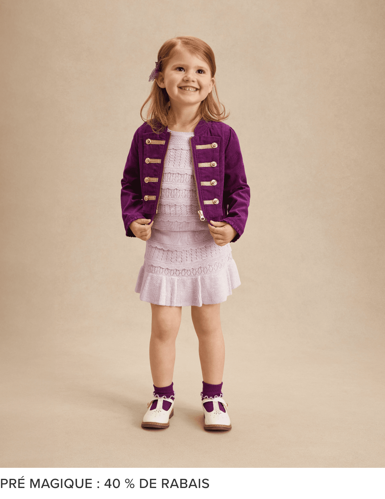 Une jeune fille aux cheveux blonds et au sourire éclatant, vêtue d'une veste violette et d'une robe blanche, se tient sur un fond beige.