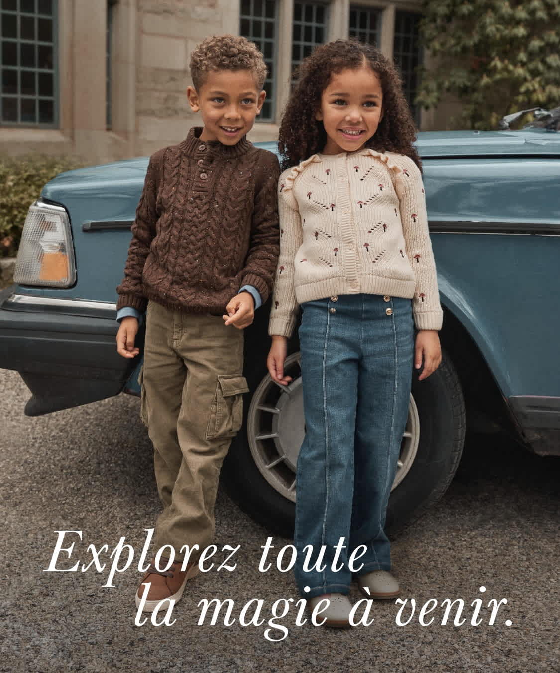 Deux jeunes gens, un garçon et une fille, se tiennent ensemble devant un vieil immeuble aux grandes fenêtres, avec une voiture de collection en arrière-plan. Le texte en surimpression invite le spectateur à « explorer toute la magie à venir ».