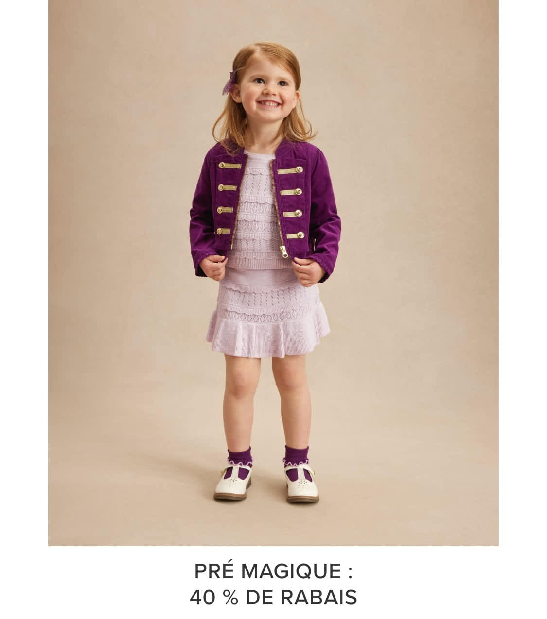 Une jeune fille aux cheveux roux et au sourire éclatant, vêtue d'une veste violette et d'une jupe blanche, se tient debout sur un fond beige uni.