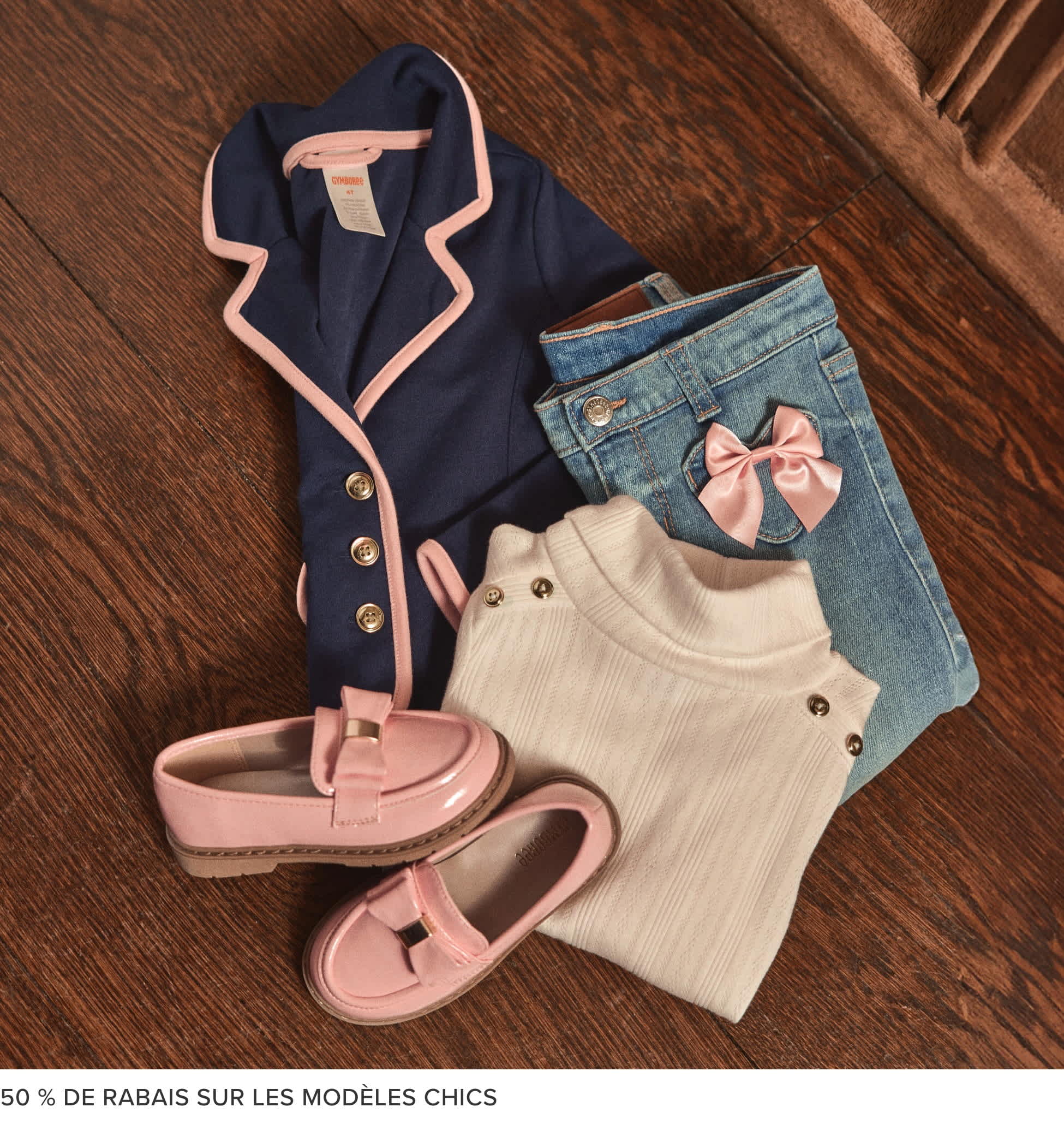 Une collection de vêtements à la mode, comprenant un manteau bleu marine, un pull blanc, un jean en denim et des sandales roses, disposés sur une surface en bois.