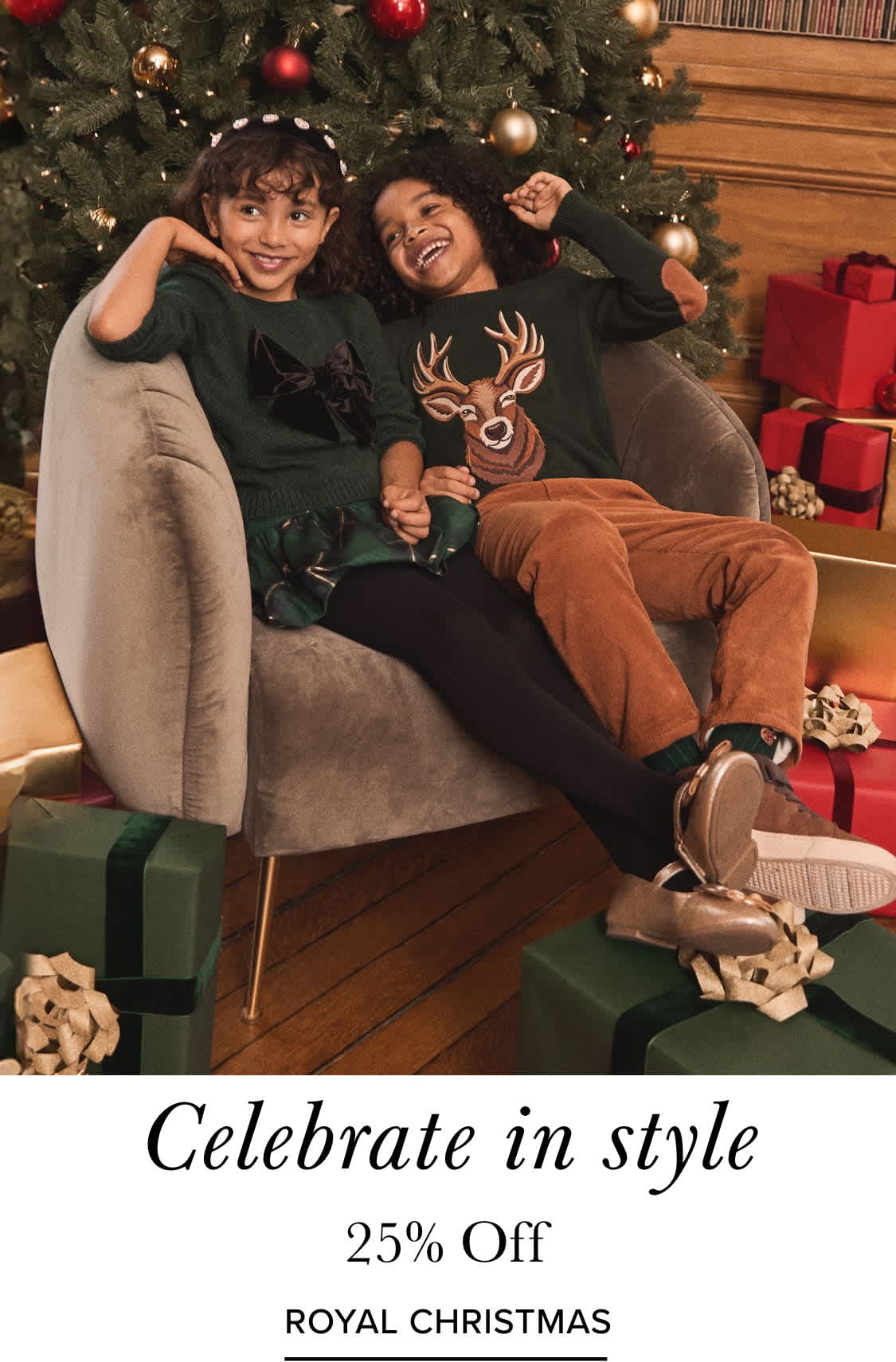 Dos mujeres jóvenes sentadas en un sofá frente a un árbol de Navidad decorado, rodeadas de diversas decoraciones navideñas y regalos.