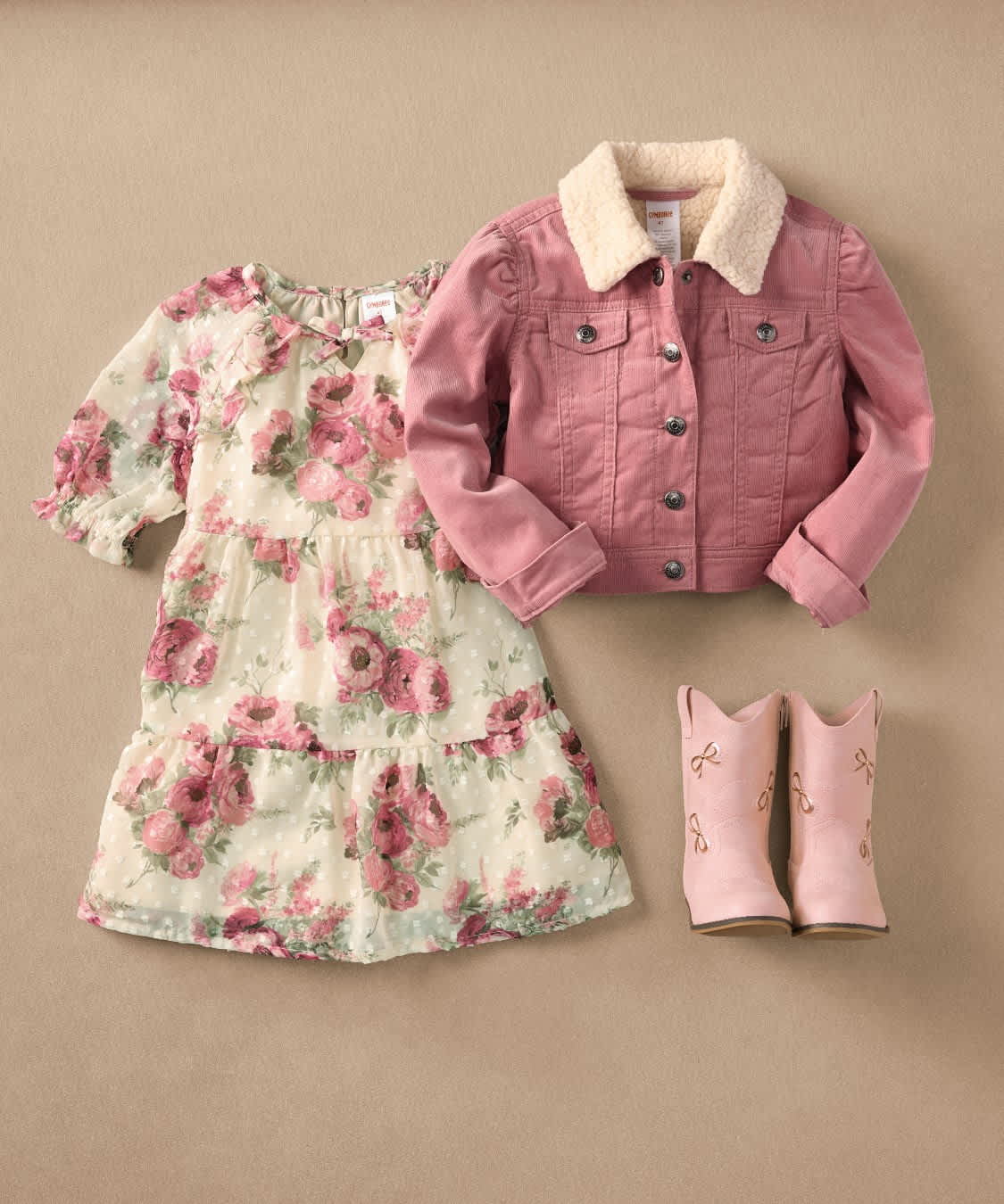 The image shows a collection of children's clothing items, including a floral print dress, a pink denim jacket with a fuzzy collar, and a pair of pink cat-themed rain boots, all arranged on a beige background.