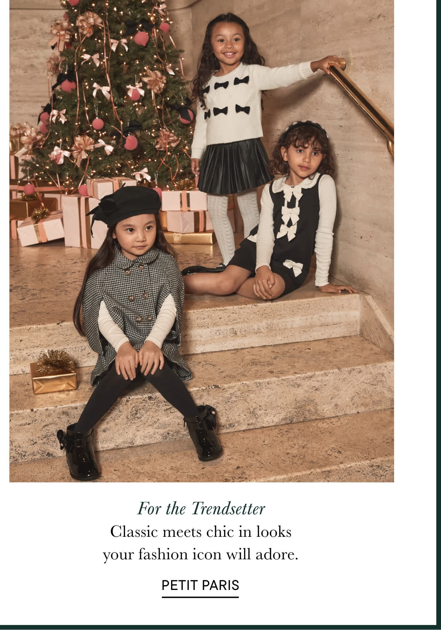 La imagen muestra a tres niños pequeños sentados en unas escaleras frente a un árbol de Navidad decorado, con el texto "Para los que marcan tendencia. Lo clásico se une a lo chic en looks que tu icono de la moda adorará. PETIT PARIS" debajo.