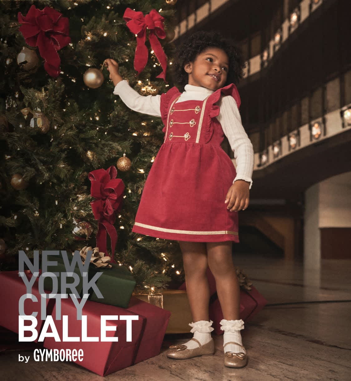 A young girl in a red dress stands in front of a Christmas tree, surrounded by holiday decorations and gifts.