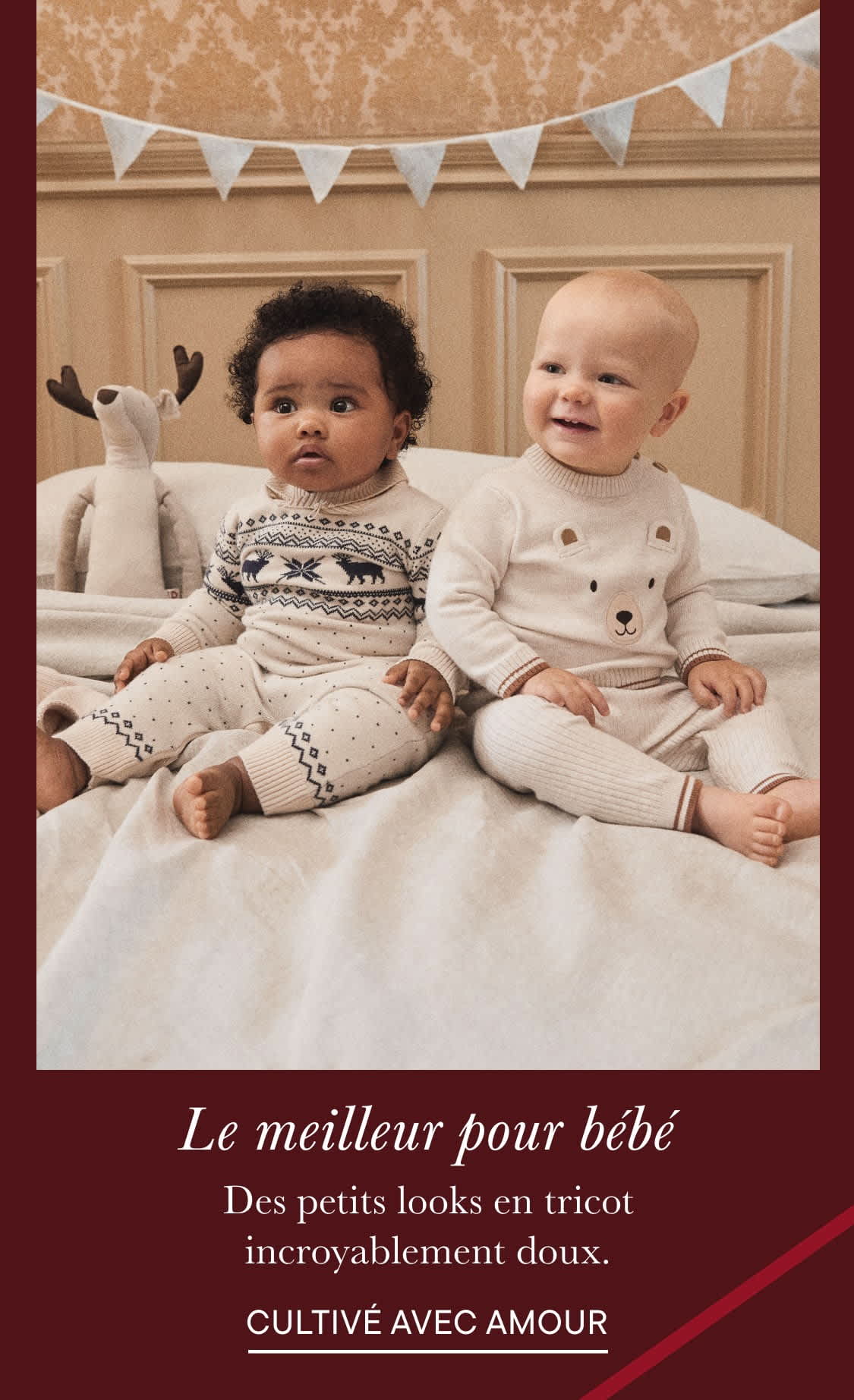 Deux jeunes enfants, un garçon et une fille, sont assis côte à côte sur un lit entouré de drapeaux ou de bannières décoratives. Ils portent tous deux des vêtements en tricot doux à motifs et semblent sourire et interagir l'un avec l'autre.