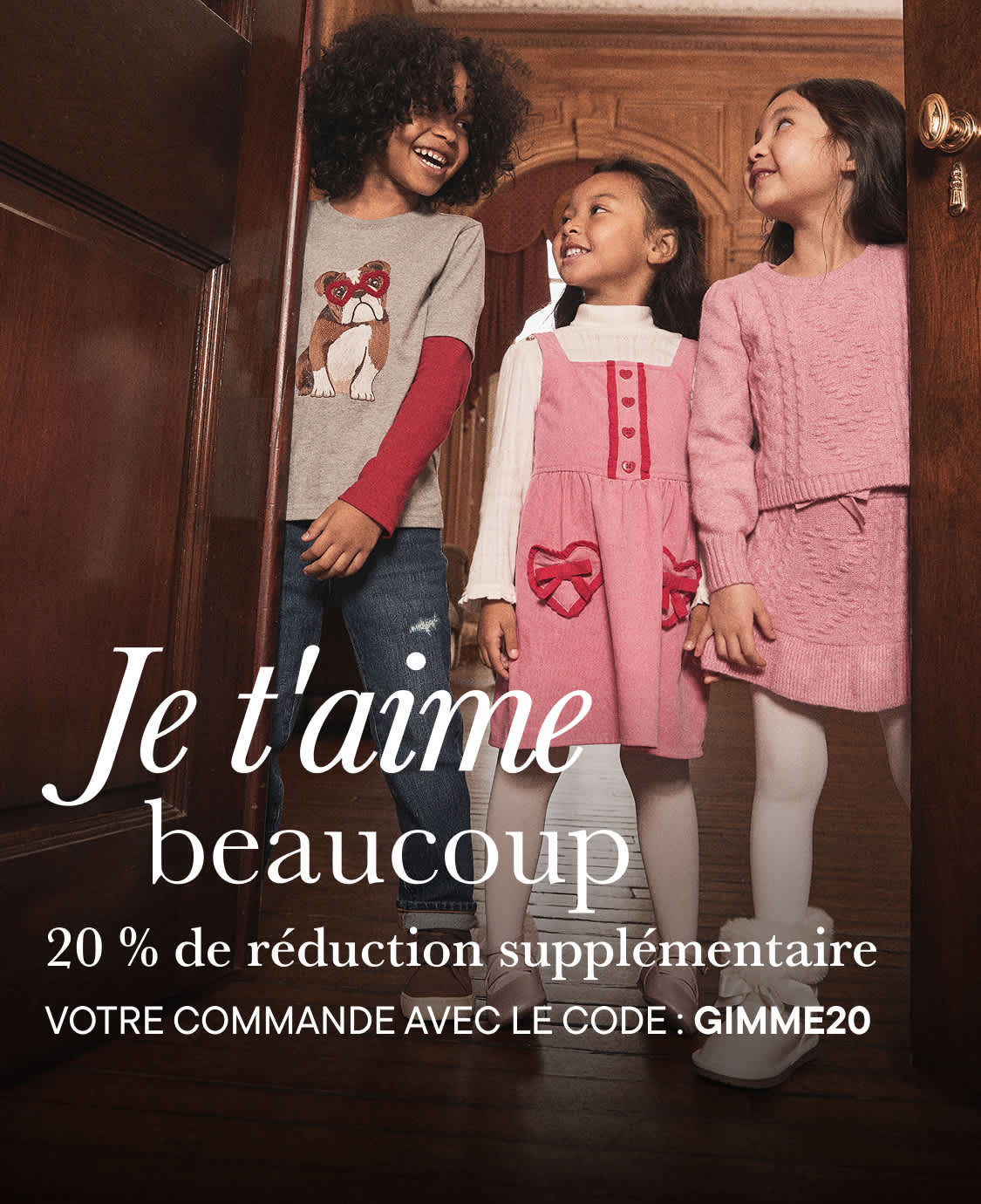 L'image montre trois jeunes filles, dont deux sourient et une qui semble rire, debout devant une étagère en bois avec une pancarte où l'on peut lire « Je t'aime beaucoup ». Les filles portent des vêtements décontractés, notamment un pull gris à motifs et une robe rose.