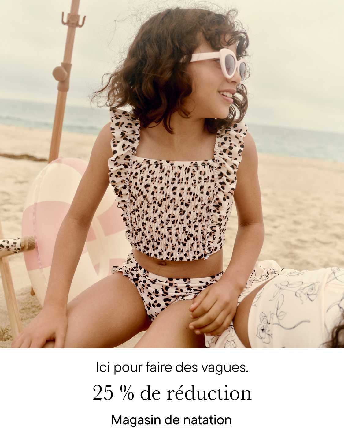Une jeune femme en maillot de bain à imprimé léopard est assise sur une plage, souriante et prête à faire des vagues, comme l'indique le texte « Ici pour faire des vagues » en arrière-plan.