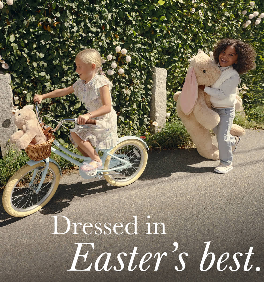 The image shows two individuals, a woman and a man, dressed in casual attire, standing next to a bicycle in a lush, green outdoor setting.