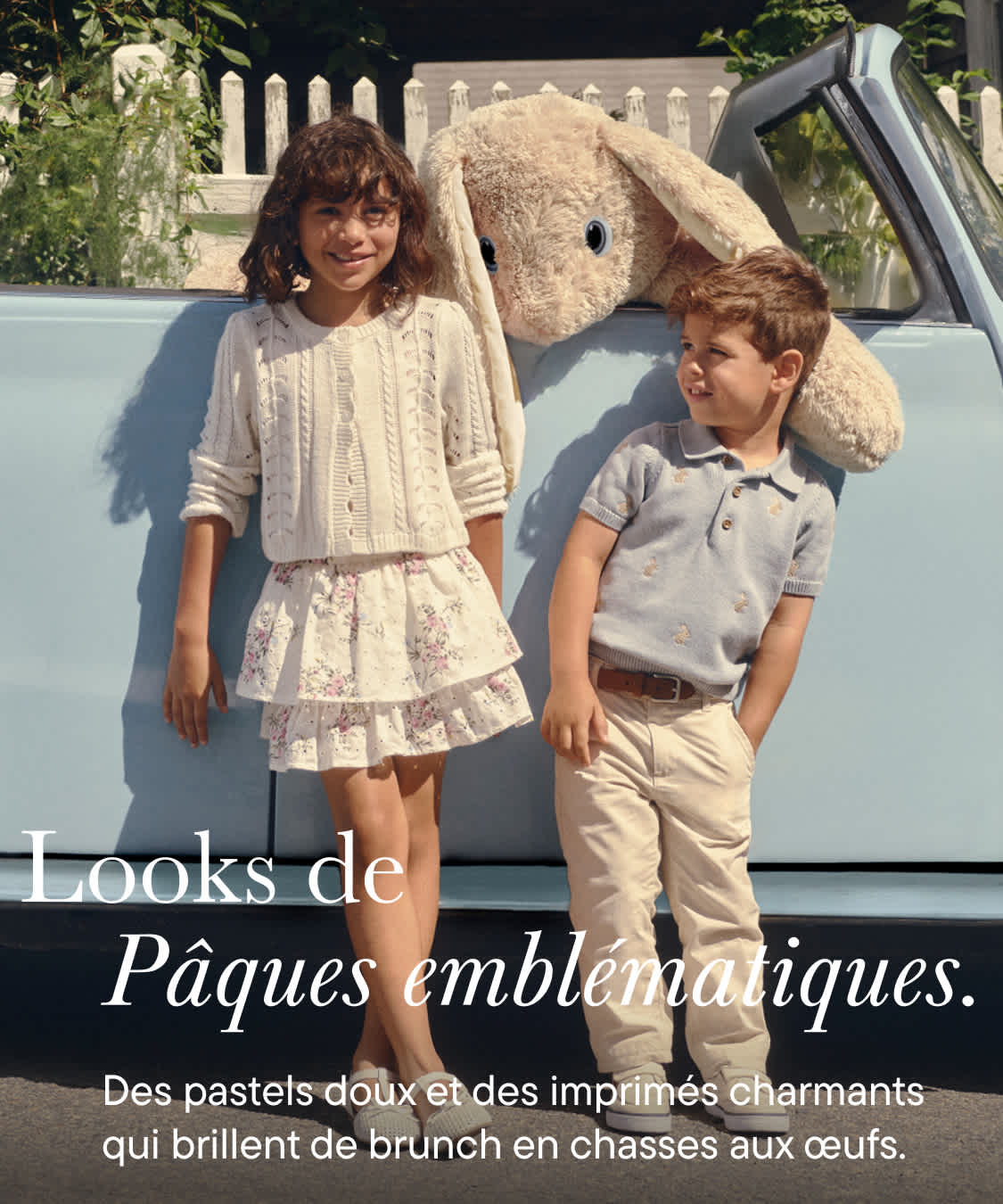 Un groupe de jeunes gens, vêtus de vêtements clairs à motifs floraux, se tiennent devant une clôture blanche, un véhicule étant visible en arrière-plan.