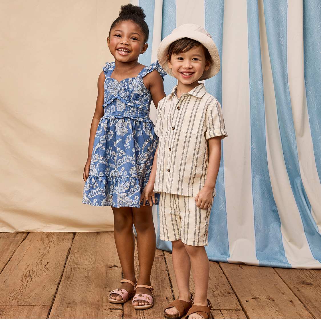 Two young women in casual summer dresses stand in front of a curtain backdrop, with a sign advertising "New Collections" in the background.