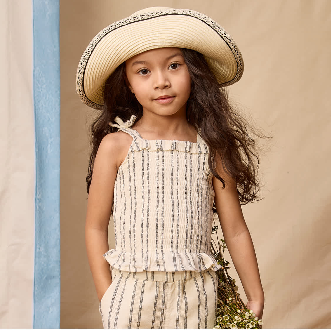 A young girl wearing a straw hat and a striped dress stands in front of a sign advertising new clothing collections.