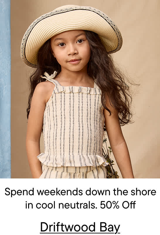 A young girl in a straw hat and striped top stands in the foreground against a neutral, textured background with a hint of blue fabric on the left.