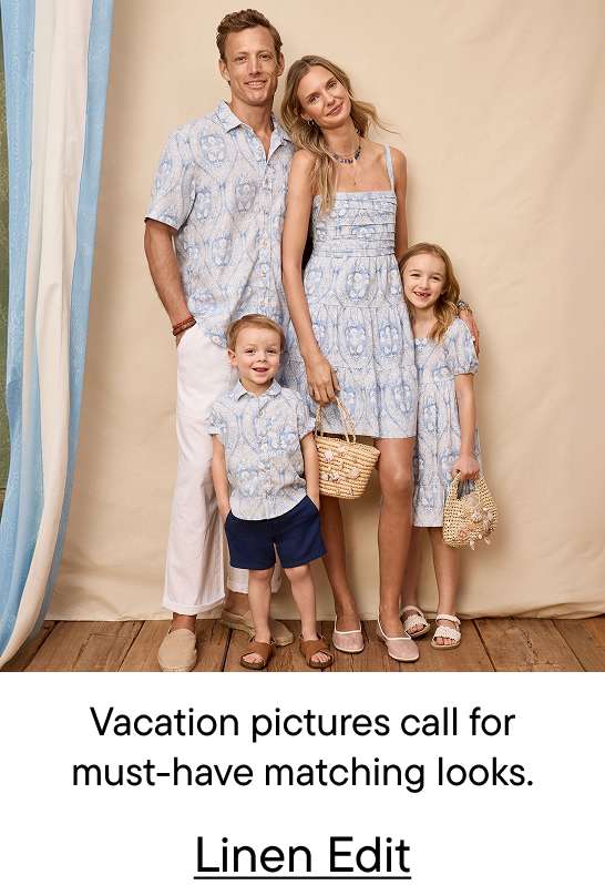 A family of four, dressed in matching blue and white patterned outfits, poses in front of a neutral backdrop with draped blue and white fabric on the left.
