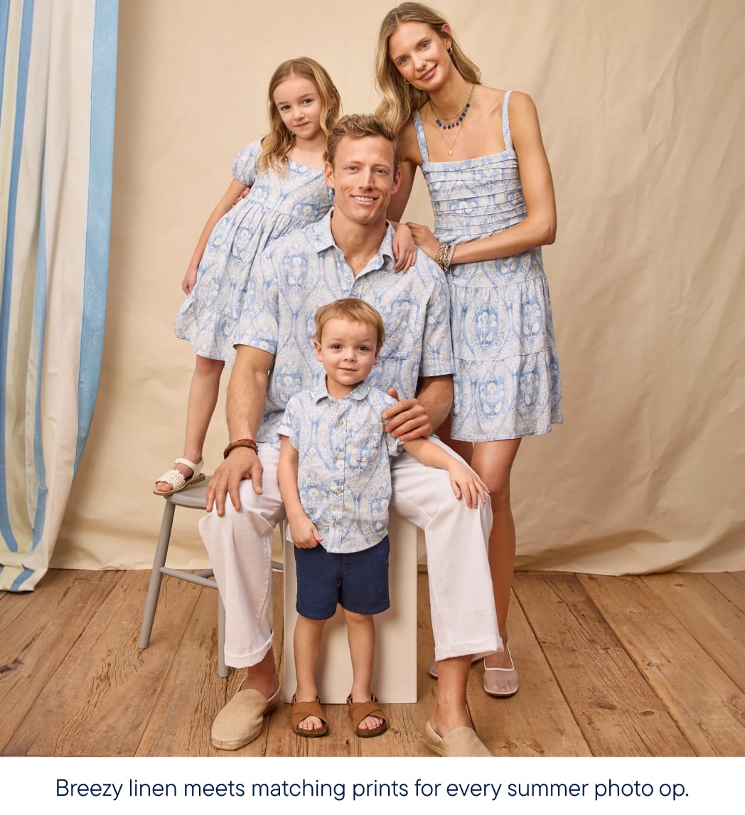 A family of four, dressed in matching blue and white patterned outfits, poses in front of a light-colored backdrop with striped curtains.