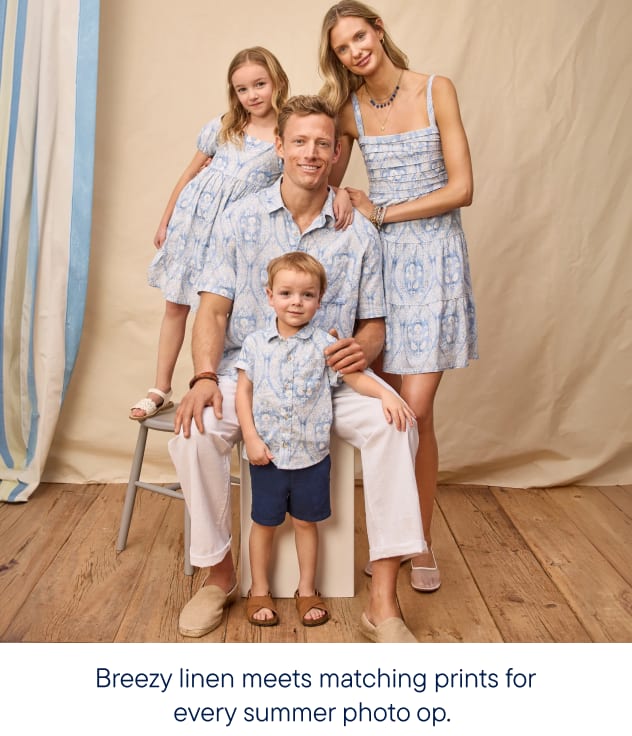 A family of four, dressed in matching blue and white patterned outfits, poses in front of a light-colored backdrop with striped curtains.