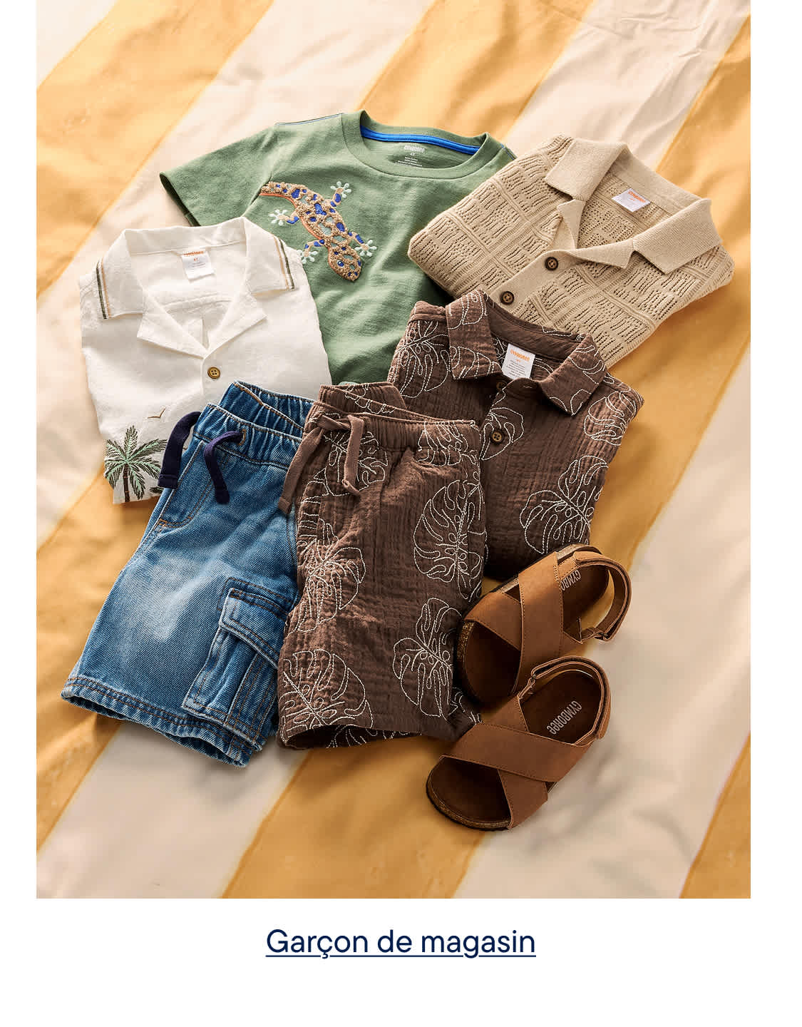 Une collection de vêtements d'été pour enfants, comprenant des shorts, des chemises et des sandales, est disposée sur un fond rayé jaune et blanc.