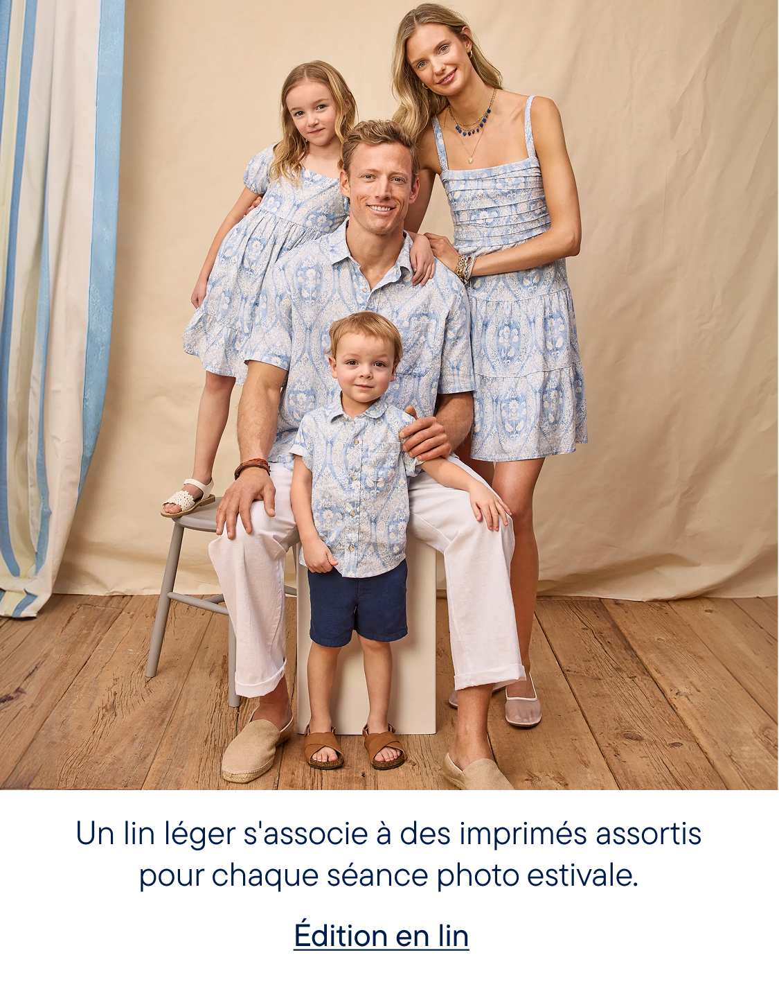 Une famille de quatre personnes, vêtues de tenues assorties à motifs bleus et blancs, pose devant un fond clair à rayures verticales bleues.