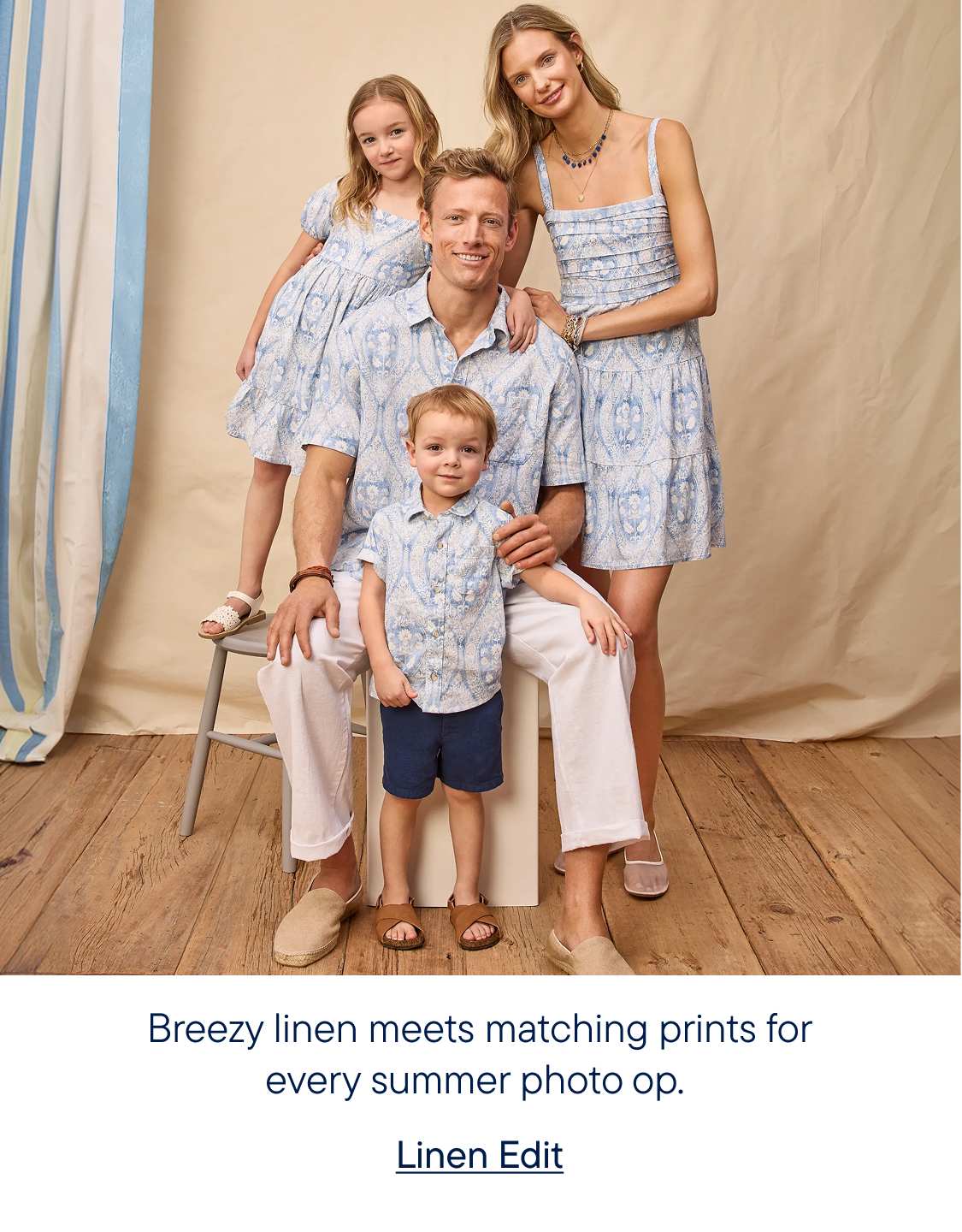 A family of four, dressed in matching blue and white patterned outfits, poses in front of a light-colored backdrop with vertical blue stripes.