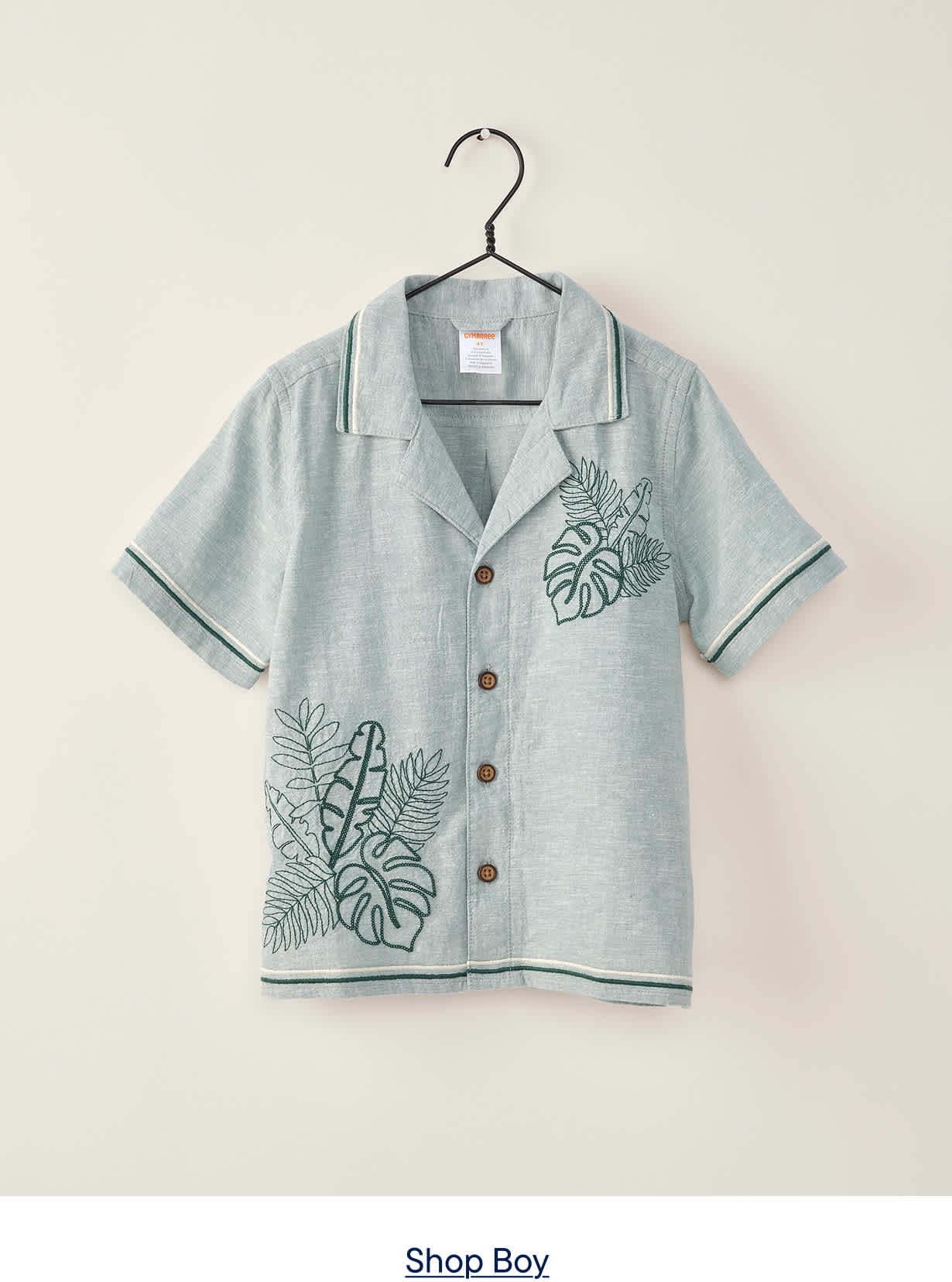 A light blue short-sleeved shirt with green leaf embroidery hangs on a black hanger against a plain, light gray background.