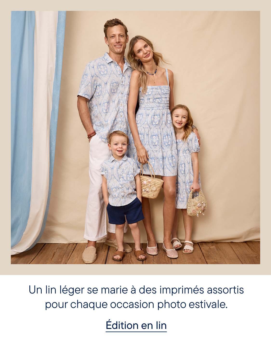 Une famille de quatre personnes, vêtues de tenues assorties à motifs bleus et blancs, pose devant un fond beige clair avec des rideaux à rayures bleues et blanches sur la gauche.
