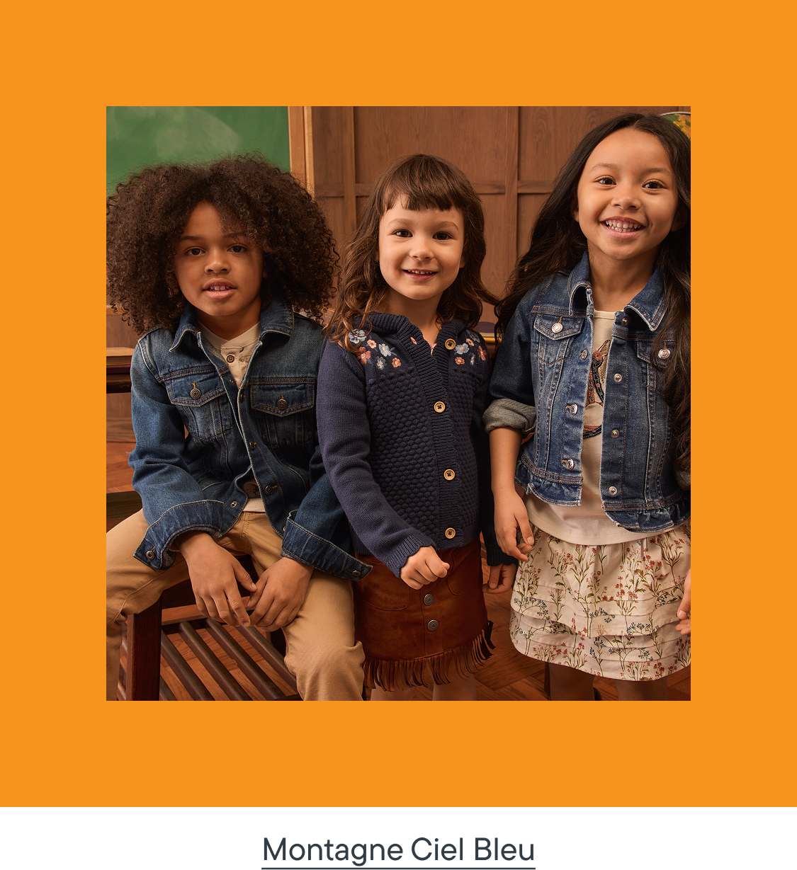 Trois enfants souriants, vêtus de tenues décontractées, posent devant un fond en bois.