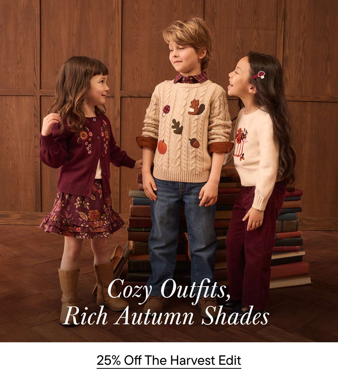 Three children dressed in autumn clothing stand together in the foreground against a background of wood-paneled walls and a stack of books.