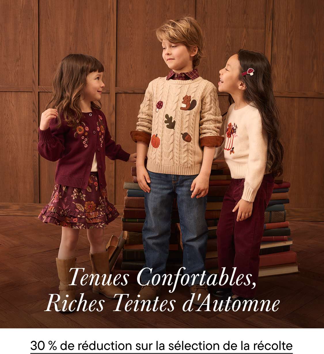 Trois enfants vêtus de vêtements aux couleurs de l'automne se tiennent ensemble au premier plan, devant un décor de pièce lambrissée et une pile de livres.