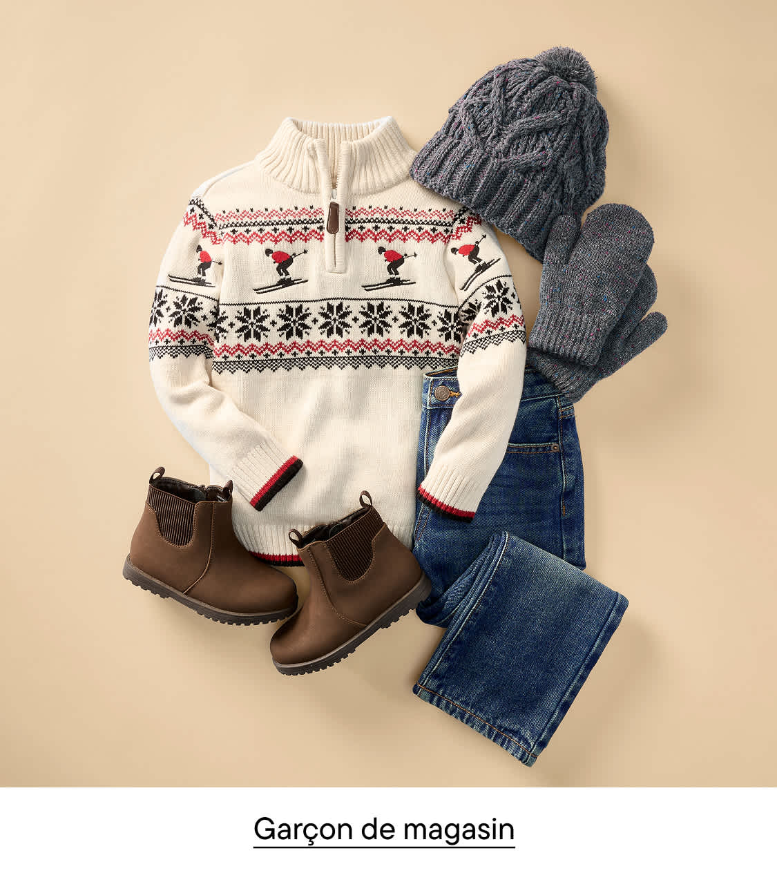 Un pull blanc à motifs, un jean bleu, des bottes marron, un bonnet et des gants en tricot gris sont disposés sur un fond beige uni.