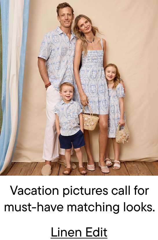 A family of four, dressed in matching blue and white patterned outfits, poses in front of a neutral backdrop with draped blue and white fabric on the left.