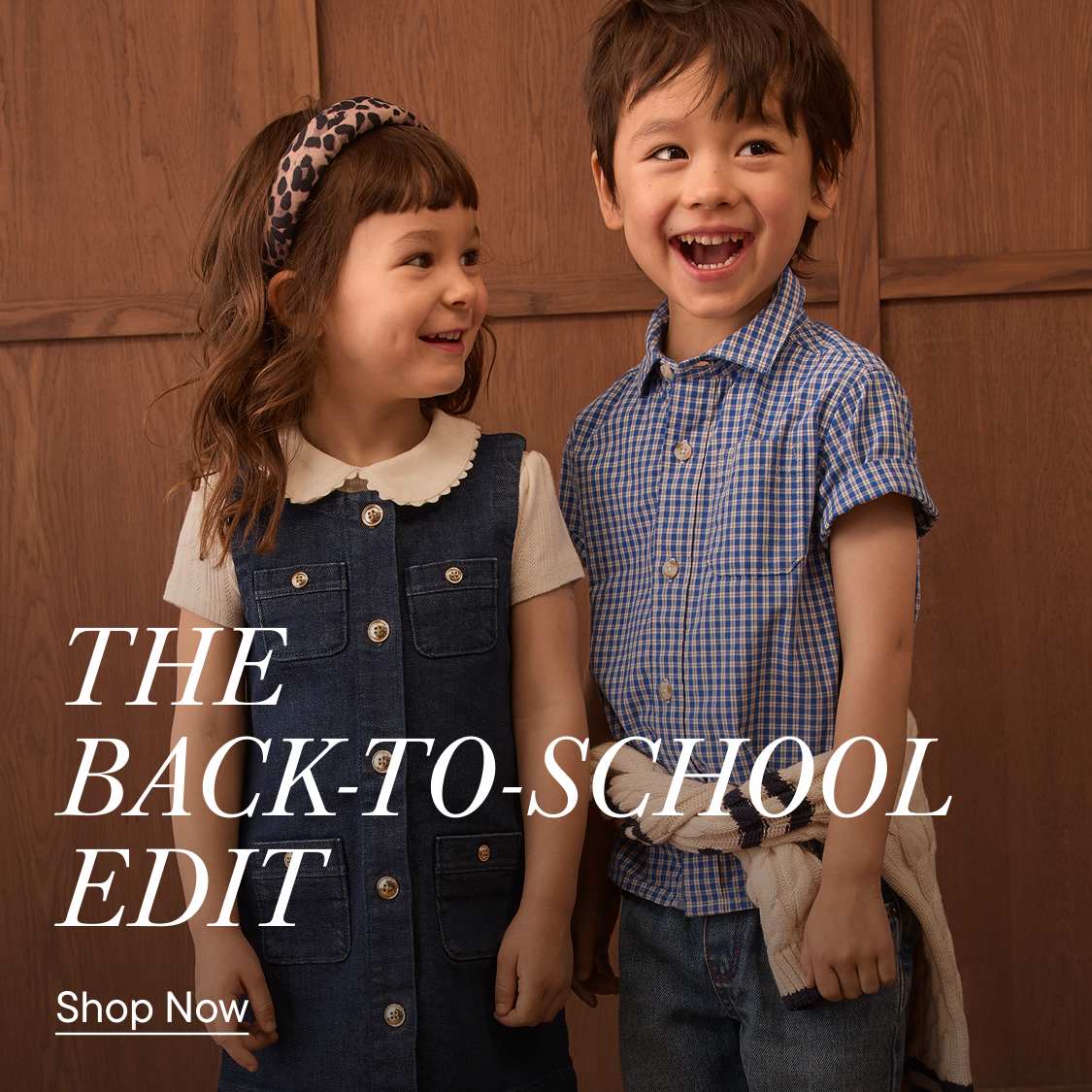Two smiling children, a girl in a denim dress and a boy in a blue gingham shirt, stand against a warm wooden background with "THE BACK-TO-SCHOOL EDIT" text overlay.