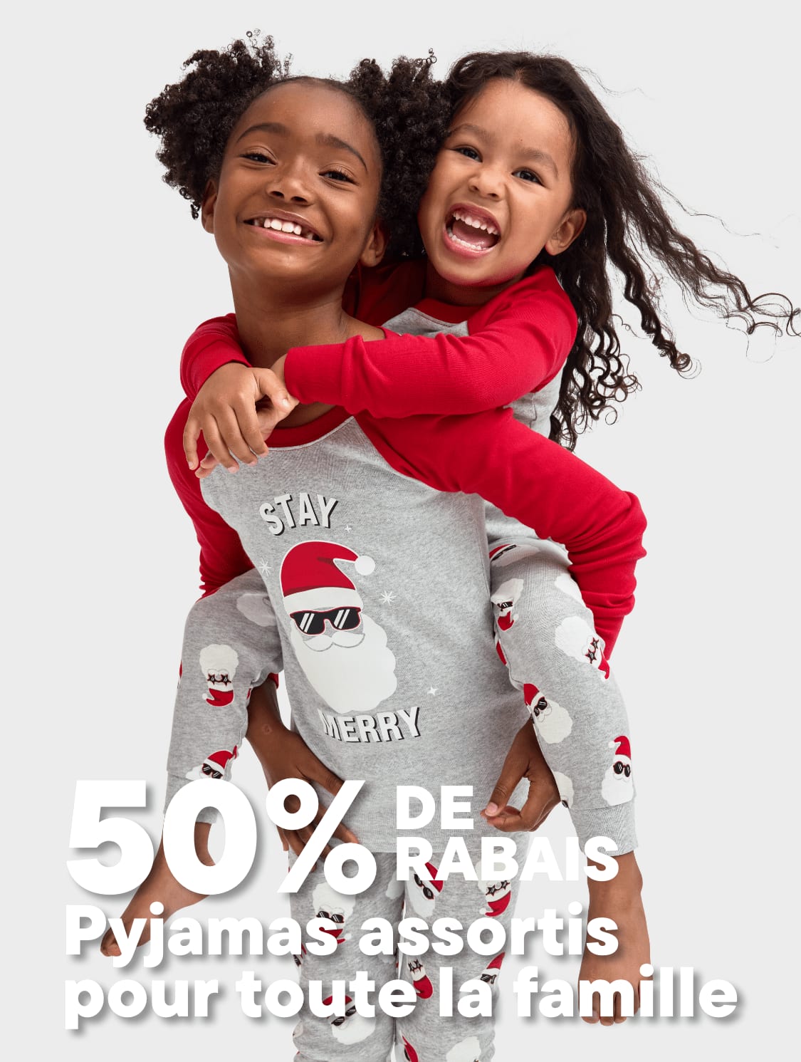 Deux jeunes filles aux cheveux bouclés portant des pyjamas rouges et gris assortis s'embrassent et sourient joyeusement sur un fond blanc uni.
