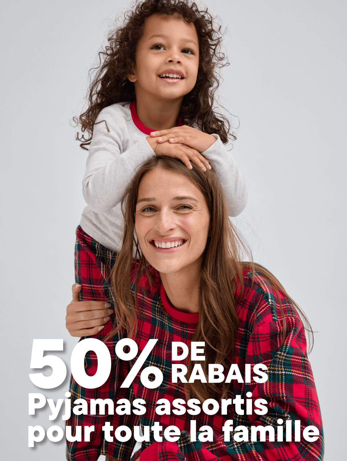 L'image montre deux jeunes filles, l'une aux cheveux bouclés, embrassant l'autre qui sourit largement, sur un fond uni avec une promotion de 50 % de réduction sur des pyjamas familiaux assortis.