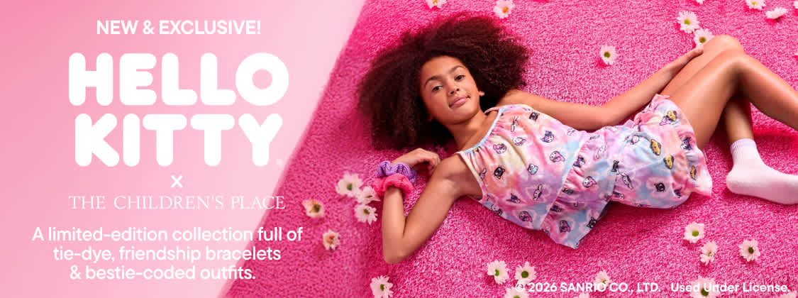 A young girl with curly hair is smiling and posing in front of a pink background with floral designs.
