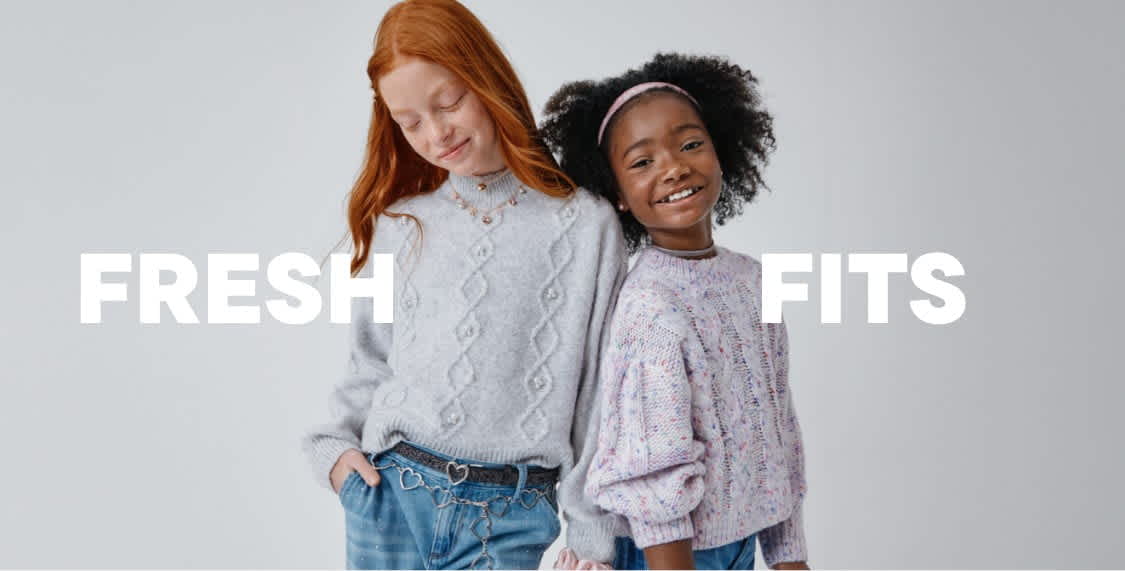 Two young women, one with red hair and the other with curly dark hair, are standing together and smiling in front of a plain white background. The text "RESH FITS" is prominently displayed above them.