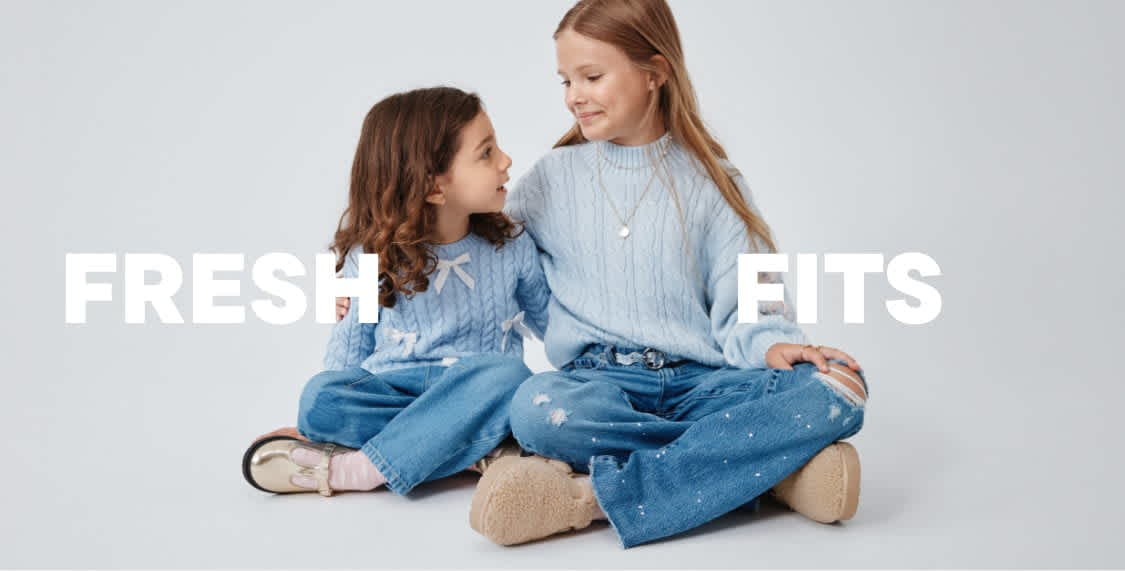 Two young women wearing casual, denim-based outfits are sitting together in the foreground, with the text "FRESH FITS" displayed prominently in the background.