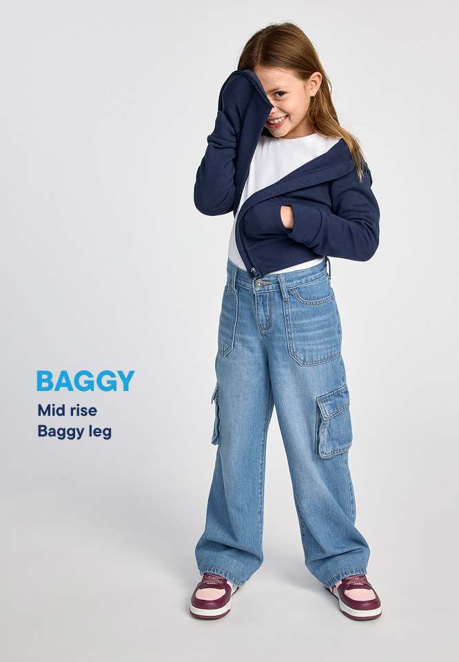 A young girl in baggy jeans and a navy jacket stands against a plain white background, with the word "BAGGY" in blue text to her left.