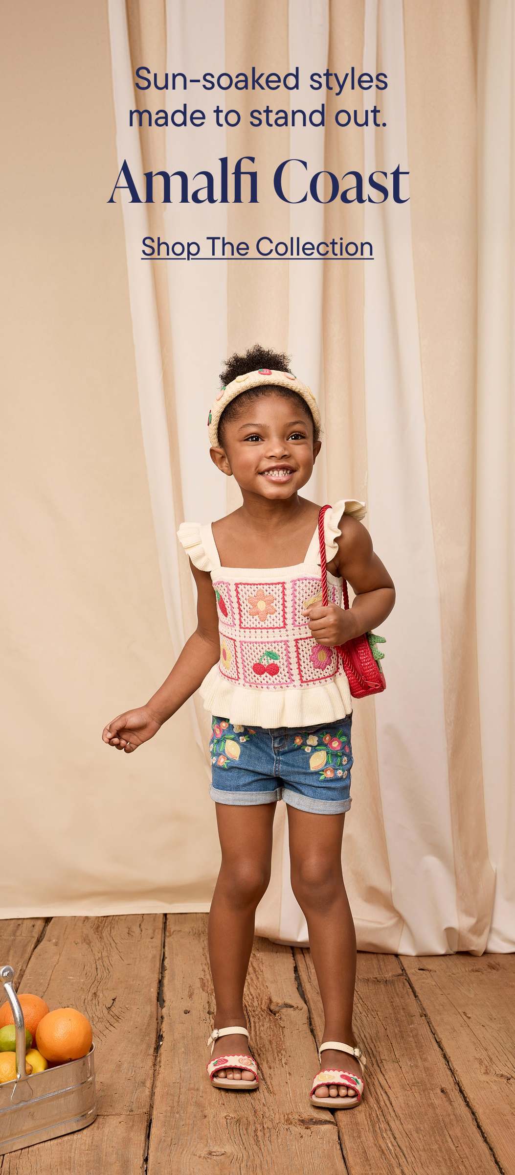 A young girl wearing a patterned top and denim shorts stands in front of a banner advertising "Amalfi Coast" fashion styles.