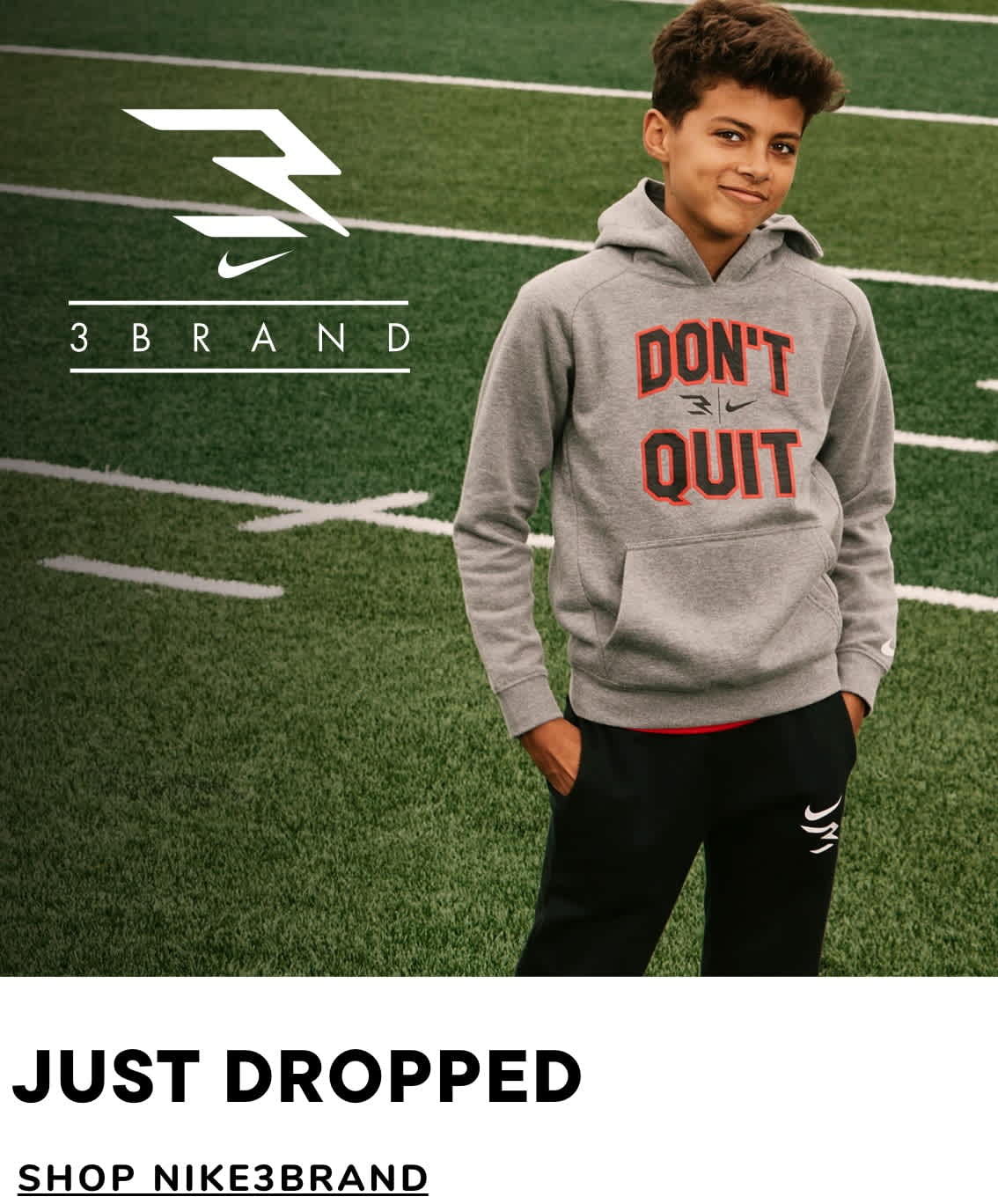 The image shows a young person wearing a gray hooded sweatshirt with the text "DON'T QUIT" printed on it, standing on a grassy field with a Nike 3 Brand logo visible in the background.