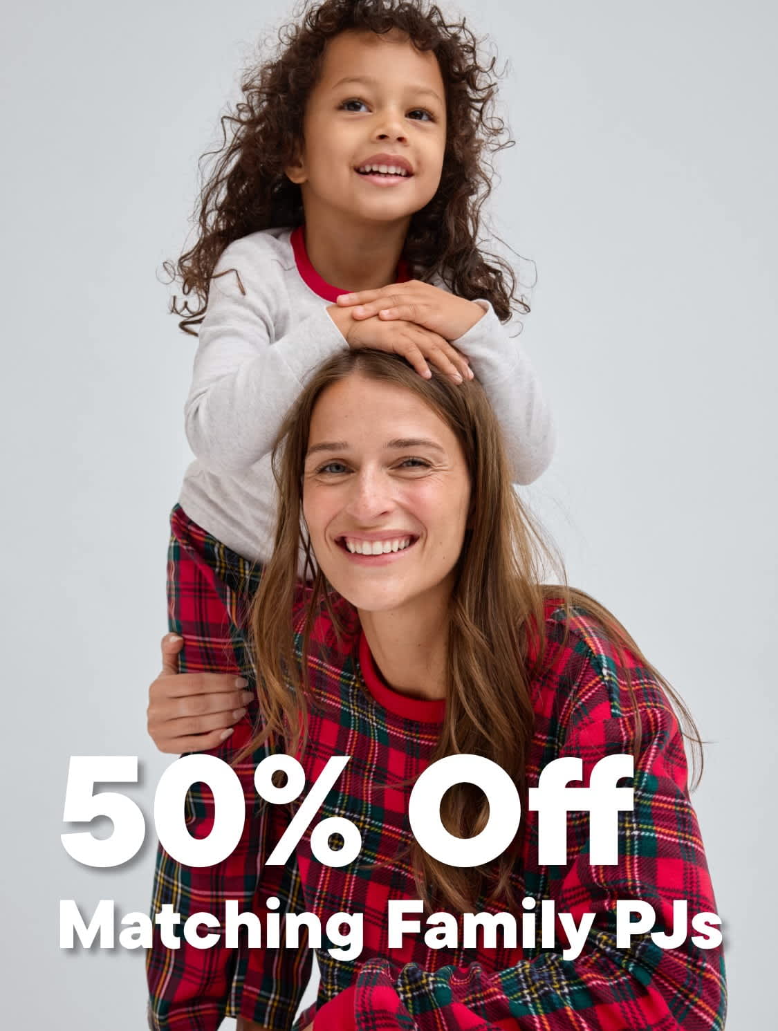 The image shows two young girls, one with curly hair embracing the other who is smiling widely, against a plain background with a 50% off promotion for matching family pajamas.