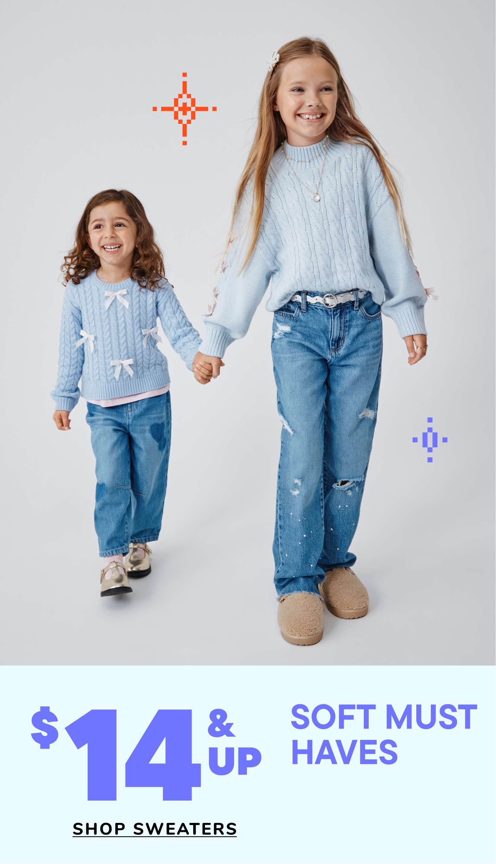 Two young girls wearing matching blue sweaters and jeans are standing together and smiling, with a "Soft Must Haves" advertisement in the background.