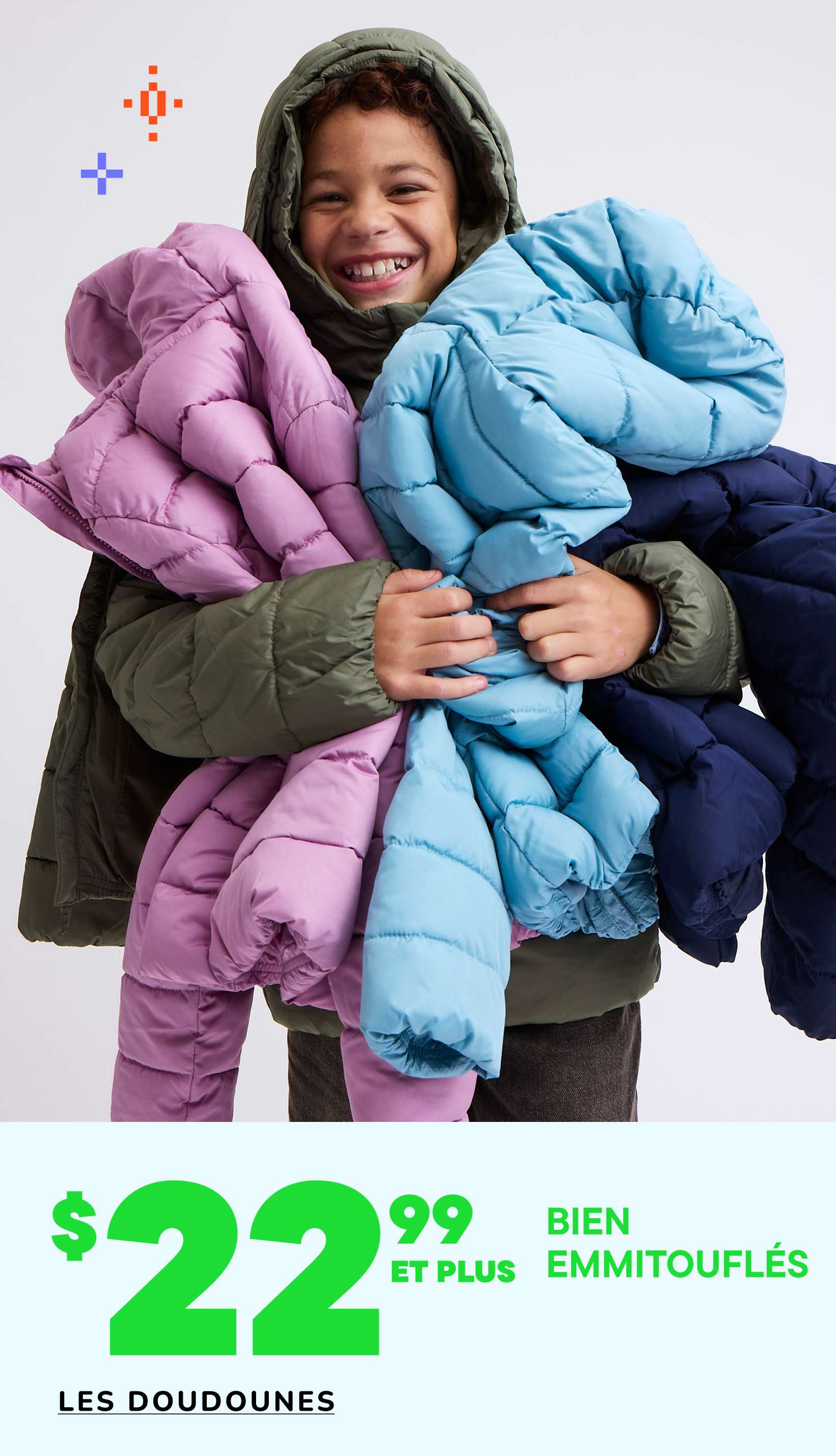 Une personne souriante, portant une veste à capuche, est entourée de diverses doudounes colorées exposées à la vente.