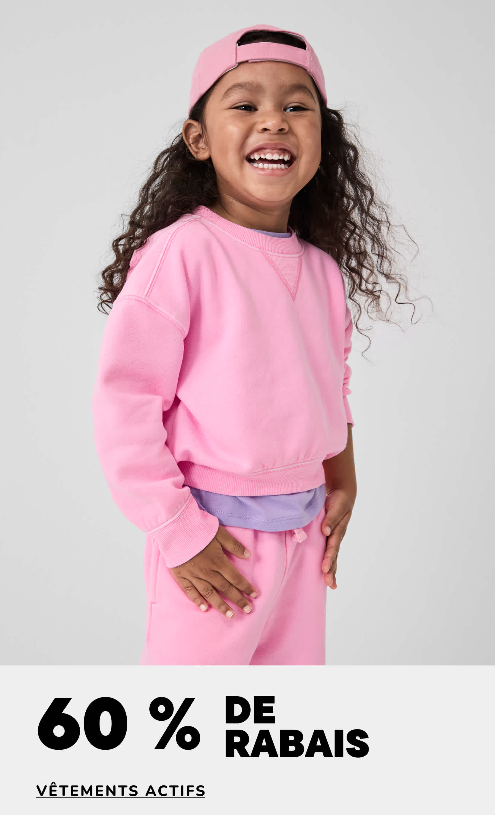 Une jeune fille aux cheveux bouclés, vêtue d'un sweat-shirt rose et d'un bandeau, sourit largement sur un fond blanc uni, avec la mention « 60 % de réduction » en surimpression.