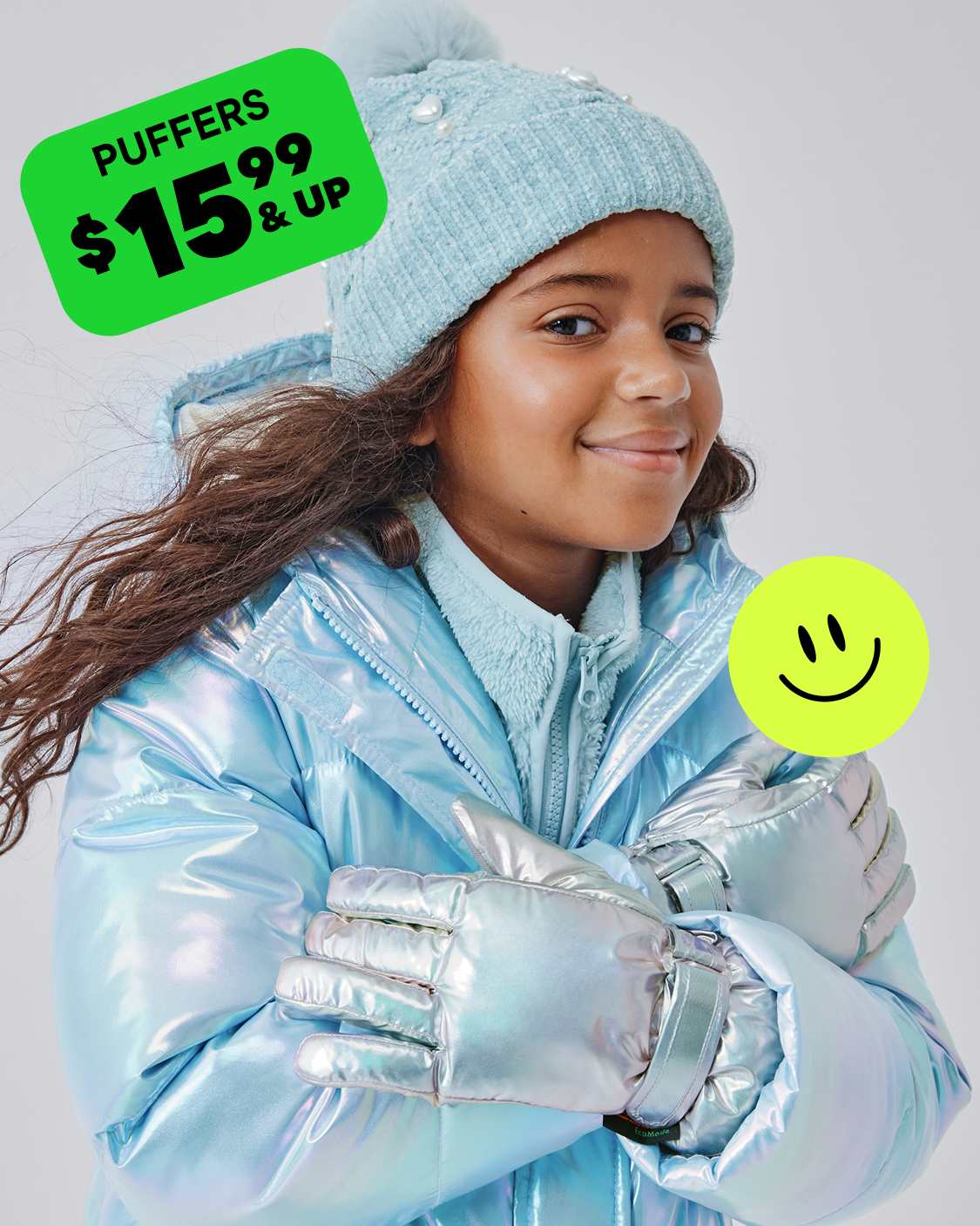 Una mujer joven, que viste una chaqueta de invierno azul claro, un gorro de punto a juego y guantes, está parada frente a un cartel verde que anuncia "Puffers $ 15,99 y más", con un ícono de cara sonriente.