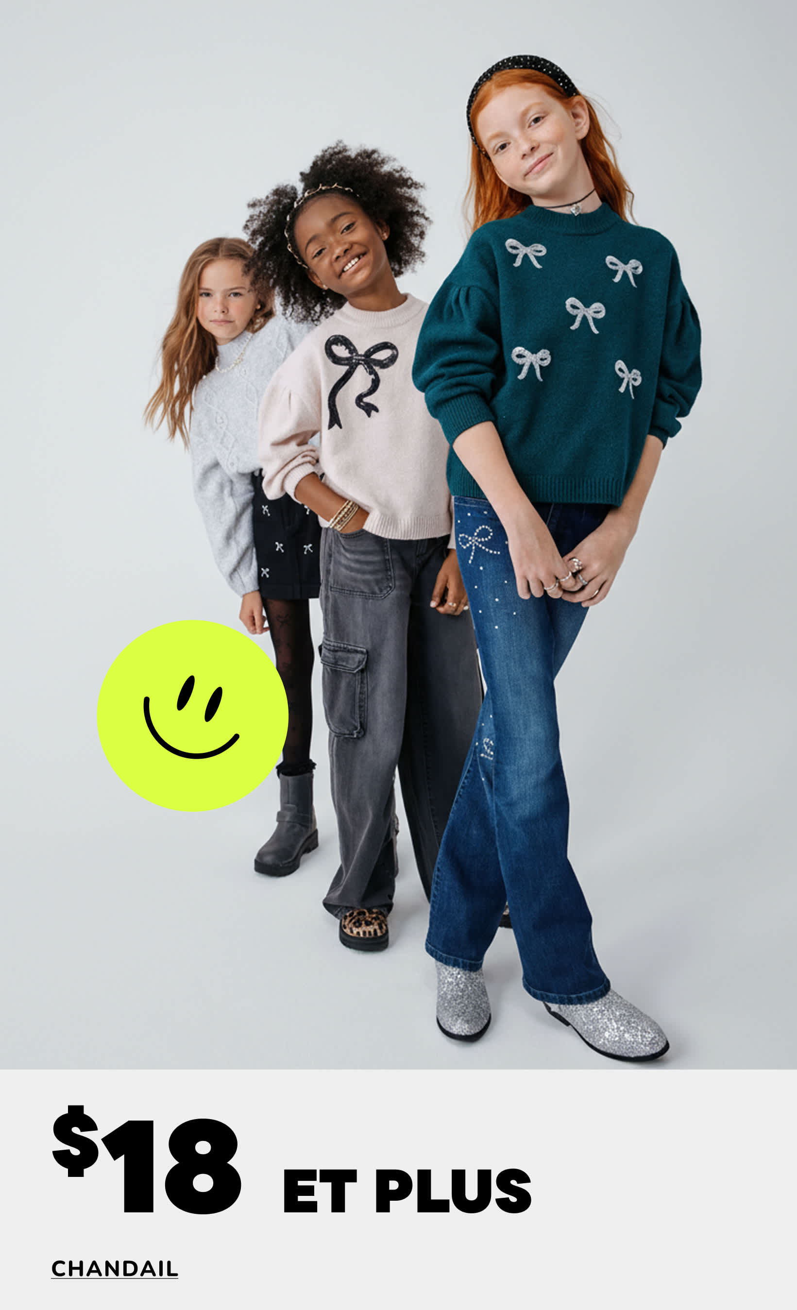 Trois jeunes filles vêtues de pulls et de jeans élégants posent ensemble dans un studio, avec un message promotionnel pour une vente de pulls affiché en arrière-plan.