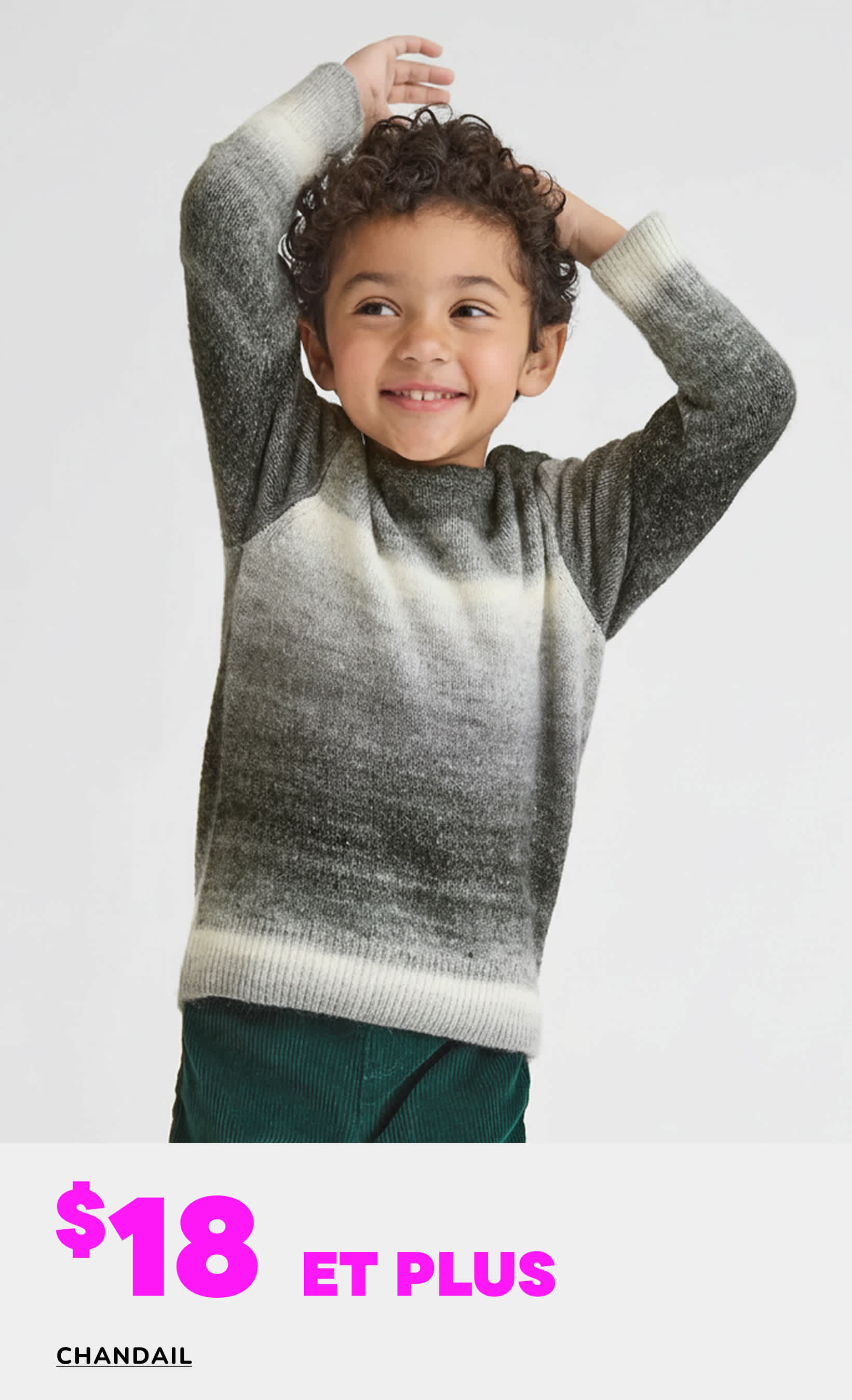 Un jeune enfant souriant aux cheveux bouclés, vêtu d'un pull gris et blanc à dégradé, se détache sur un fond blanc uni, avec un texte superposé « 18 $ et plus » annonçant une vente de pulls.