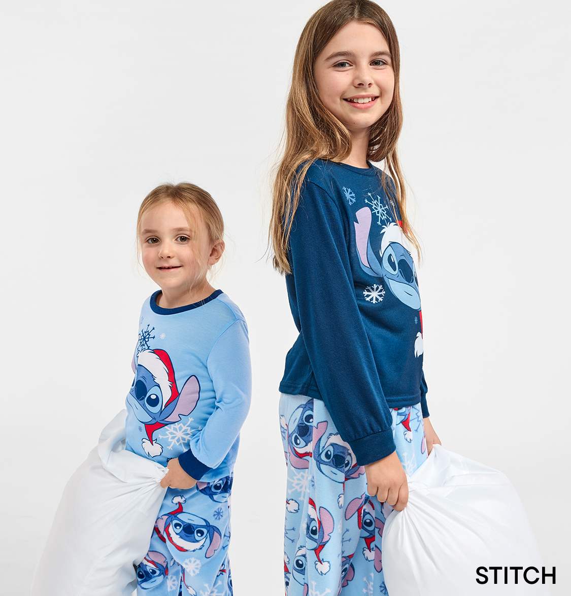 Two young girls wearing matching Stitch-themed pajamas, smiling and posing against a plain white background.