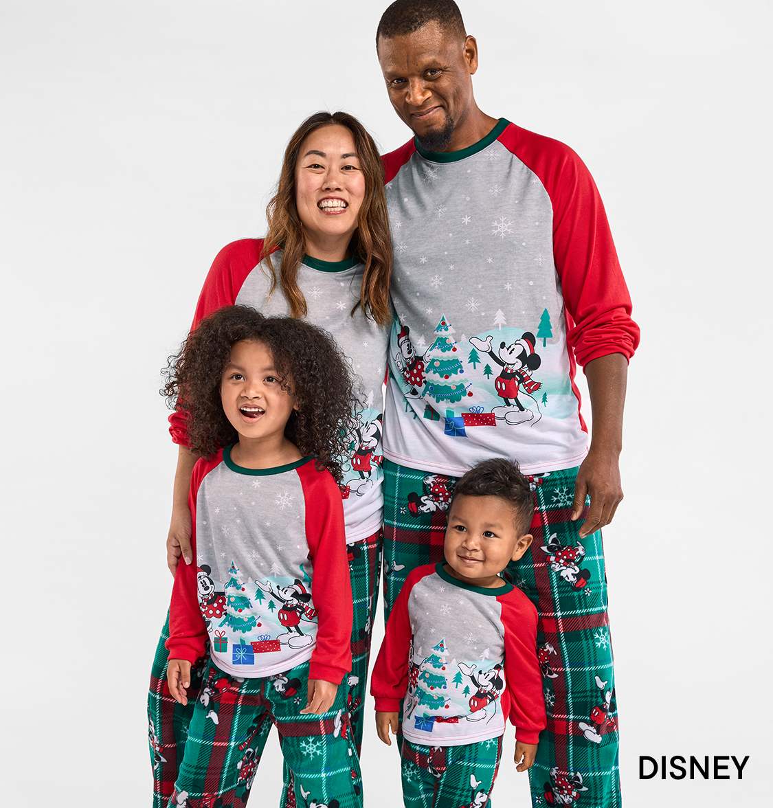A family of four, including a smiling woman, a man, and two children, wearing matching holiday-themed pajamas against a plain white background.
