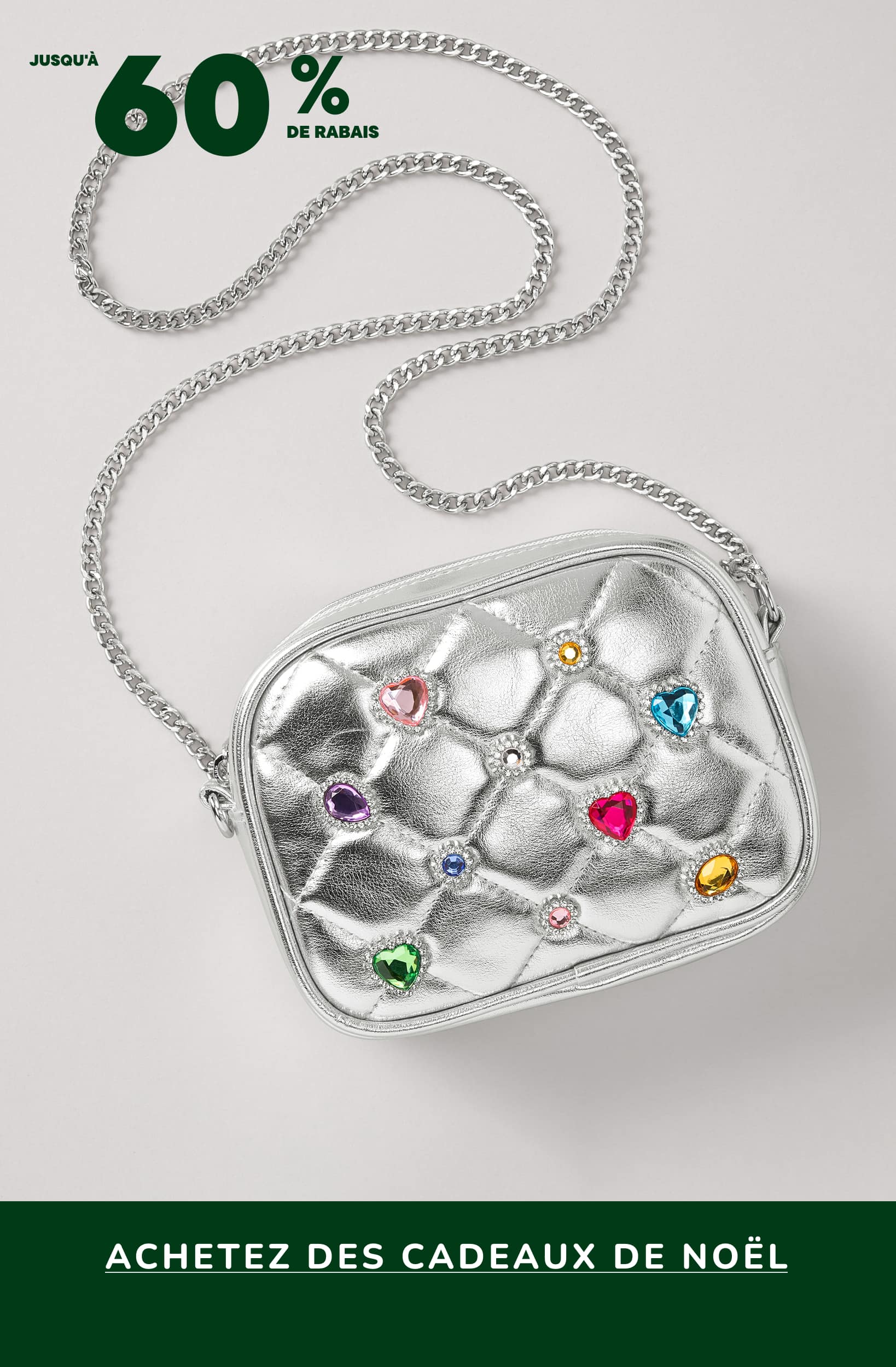Un sac à main ou une pochette argentée métallisée ornée de pierres précieuses ou de cristaux colorés, sur fond blanc uni avec une bannière verte annonçant une vente de petits cadeaux de Noël.