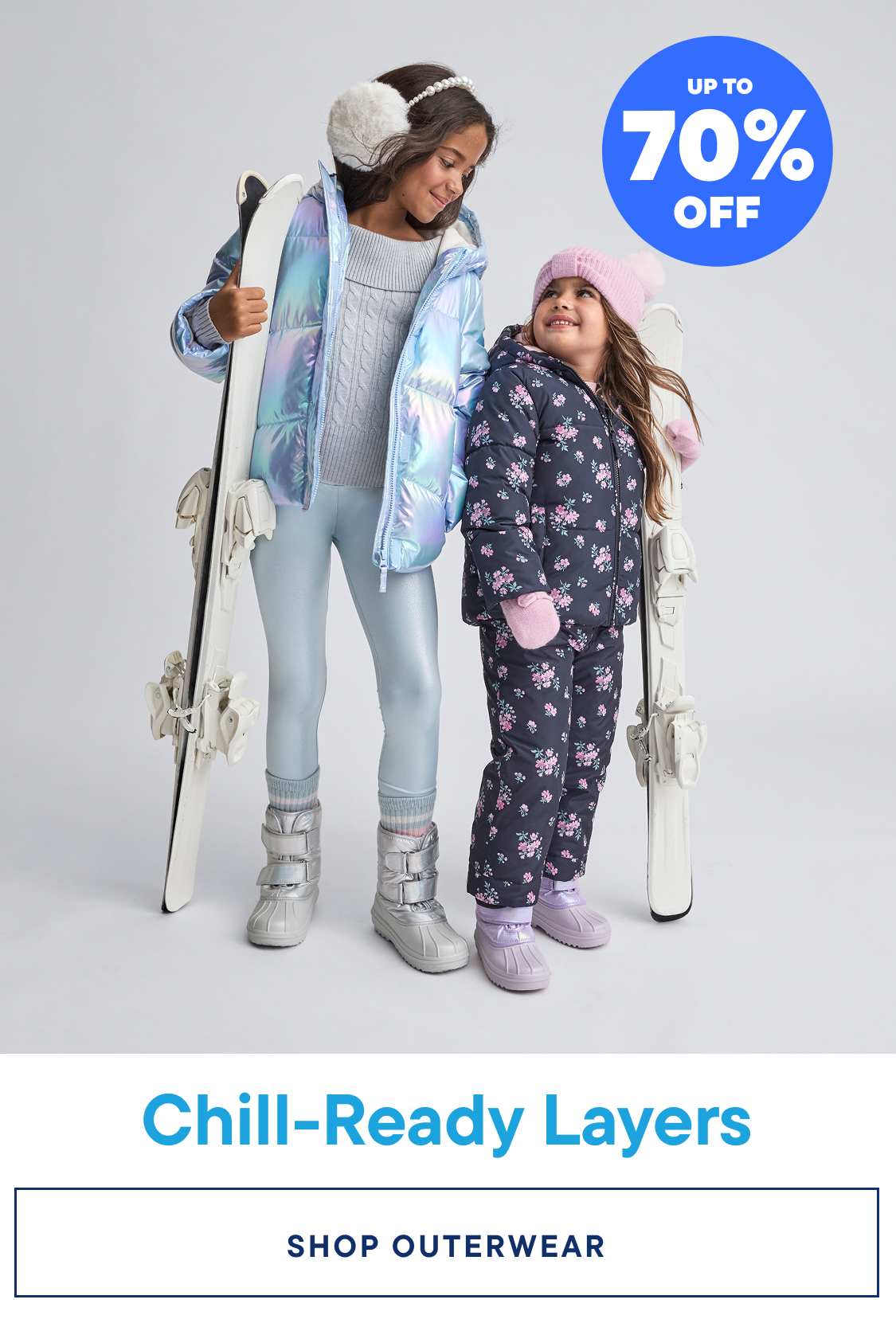 Two young girls wearing colorful winter outfits, including puffy jackets and snow pants, standing in front of a plain background with a promotional banner advertising "Chill-Ready Layers" and "Up to 70% Off" on graphic tees.